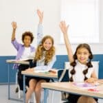 Engaged students in a diverse classroom participate actively, raising hands with enthusiasm.